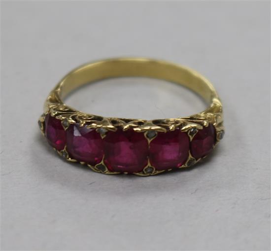 A yellow metal and graduated five stone ruby ring, with diamond chip spacers, size N.